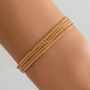 Detail of five-layer gold woven chain bracelet showing metallic texture on wrist