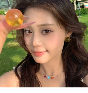 Detail of a woman wearing amber resin round studs and a colorful heart pendant necklace