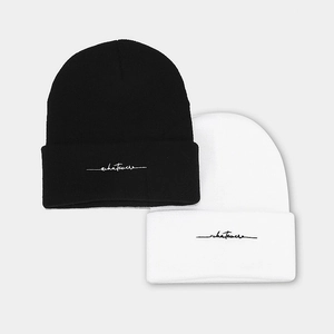 Classic black and white knit beanies with whatever embroidery in a flat lay view