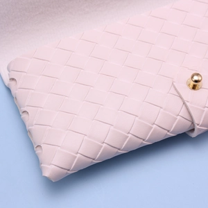Detail of woven faux leather texture and golden metal clasp on a light pink glasses case