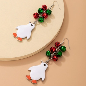 Macro detail of Christmas penguin earrings with festive red and green bells on beige pad