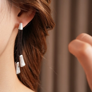 Close-up of silver earrings with dark brown suede tassels worn on model's ear