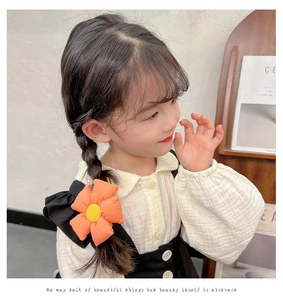 Close-up of cute orange sunflower hair tie on a child's braid with soft cotton texture