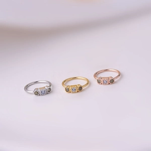 Close-up of nose rings in silver, gold, and rose gold with blue and green zircon stones
