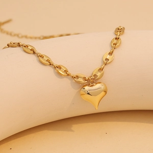 Dettaglio di una collana dorata con ciondolo a cuore e catena a maglia muso di maiale