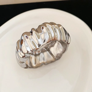 Détail d'une bague large argentée avec une texture métallique plissée unique