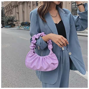 Close-up of a purple pleated cloud bag paired with a stylish blue blazer on a city street