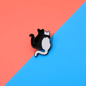 Detailed view of two cute cartoon cats hugging enamel brooch pins on a dual-tone background