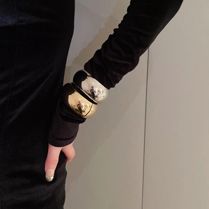 Close-up of polished gold and silver oval wide bangles on a model's wrist with black velvet