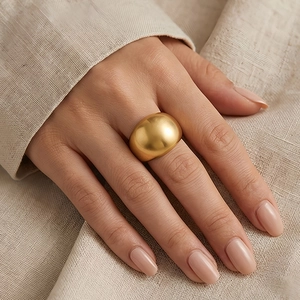 Close-up of a wide polished gold metal dome ring worn on a finger against linen