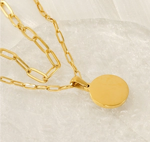 Gros plan sur la chaîne rectangulaire en acier inoxydable doré et son pendentif rond