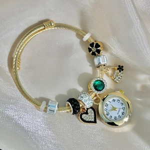 Detail of golden quartz bracelet watch featuring beaded charms and black clover pendant