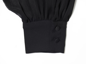 Détail de la manche d'un haut noir en mousseline avec fermeture à double bouton et plis