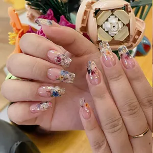 Close-up of long square nails with dried flowers and gold foil in transparent gel