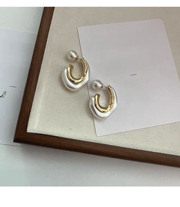 Detailed close-up of U-shaped gold metal and pearl resin earrings on a vintage tray