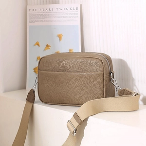 Detail of khaki pebbled leather crossbody bag with silver hardware and woven strap