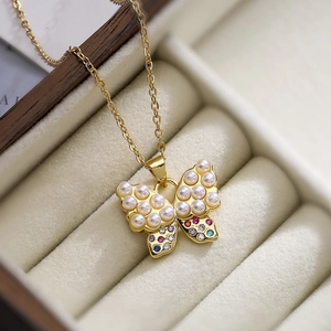 Golden butterfly necklace with pearls and multi-color zircons on a beige velvet box