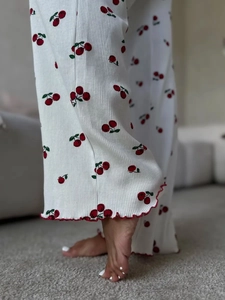 Detail of white ribbed pajama pants with cherry print and red lettuce edge hemline
