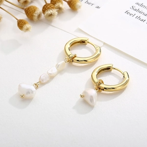 Détail de boucles d'oreilles asymétriques avec anneaux dorés et perles baroques
