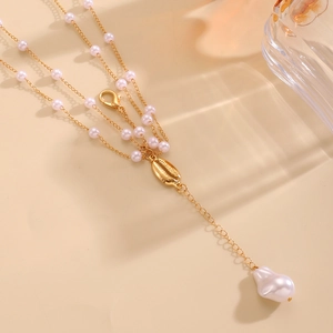 Detail of a gold layered body chain featuring faux pearls and a natural shell pendant