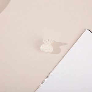 Macro detail of a rabbit-shaped hair clip with inlaid white pearls on a beige surface