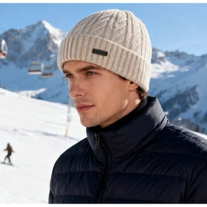 Detail of off-white chunky knit beanie featuring a leather patch on outdoor ski resort