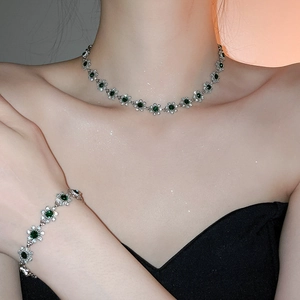 Close-up of sparkling flower pendant necklace and bracelet set with green gemstones