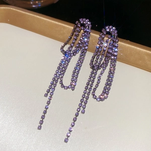 Detail of silver drop earrings with purple rhinestones and layered long tassels on a tray