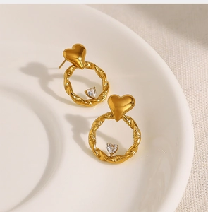 Close-up of golden twisted hoop earrings featuring a heart stud and small crystal