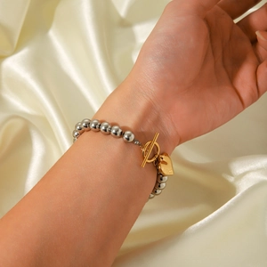Close-up of beaded bracelet with silver beads and golden heart charm on silk