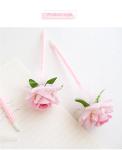 Close-up of pink fabric rose pens with white feathers and green leaves on a notebook