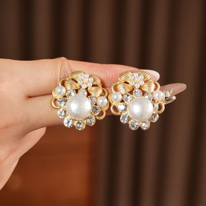 Makroaufnahme goldener Vintage-Blumenohrringe mit Perlen und Strass in der Hand