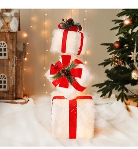 Close-up of three white snowy Christmas gift boxes with red ribbons and warm glowing lights