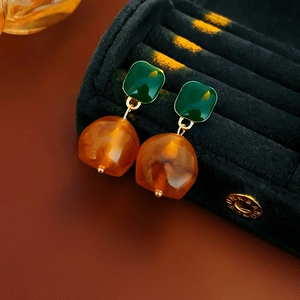 Macro detail of geometric vintage earrings with green resin square and amber-tone round drop