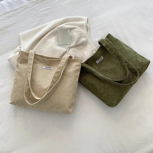 Detailed top view of large corduroy tote bags in beige and green on white bedding