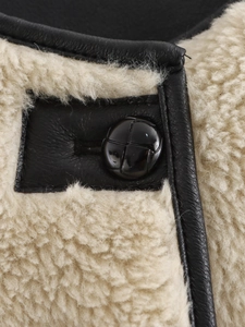 Close-up of black leather trim and soft white shearling texture with a round button