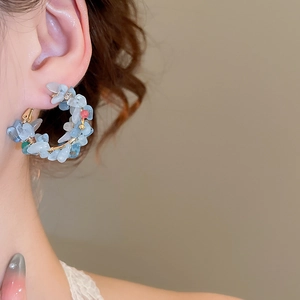 Detail view of gold hoop earrings with irregular blue gemstones and pearls on a model