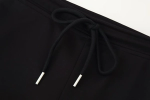Detailed view of black trousers waistband with woven drawstring and silver metal tips