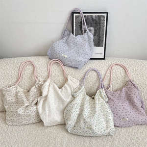 Détail de cinq sacs cabas en mousseline florale en violet, crème et bleu sur canapé