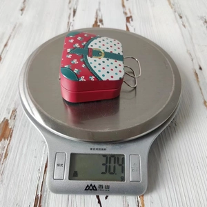 Detailed view of Christmas tin candy box on scale showing weight of 30.4g for gifting