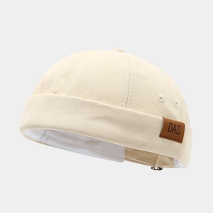 Gros plan d'un bonnet docker beige avec un détail d'écusson en cuir 'DAD' brun