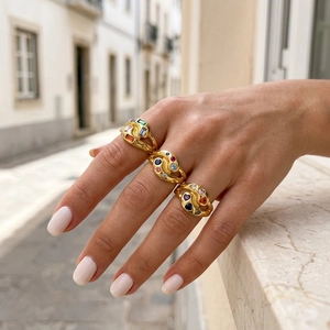 Detailed view of three vintage gold rings with multicolored gemstones on a light stone surface