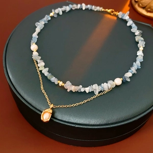 Detail of a gold shell pendant on a double-layer necklace with blue stones and pearls