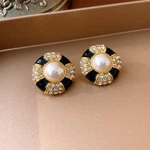 Close-up of vintage gold button earrings with black enamel, white pearl and crystal accents