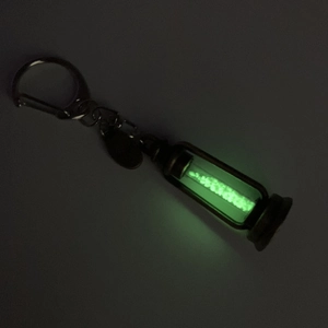 Close-up of hourglass pendant glowing with green fluorescent powder in the dark