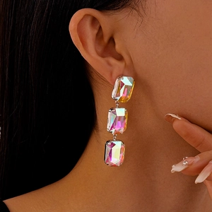 Close-up of dangling silver needle earrings featuring three rectangular iridescent stones