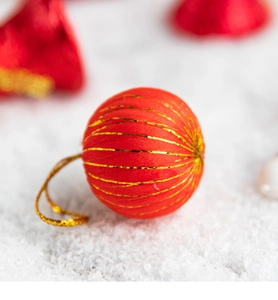 Close-up of red and gold thread-wrapped Christmas ornament on a snowy background