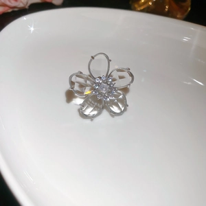 Macro detail of silver flower ear cuff with clear crystals on a white ceramic plate