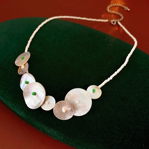 Close-up of shell necklace with iridescent discs and green beads on green velvet