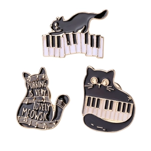 Three black cat enamel pins with piano theme and golden outlines on a white background